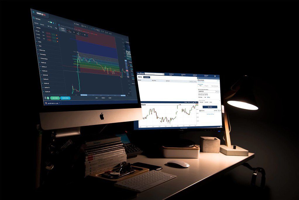 A dark desk with two monitors showing crypto price charts