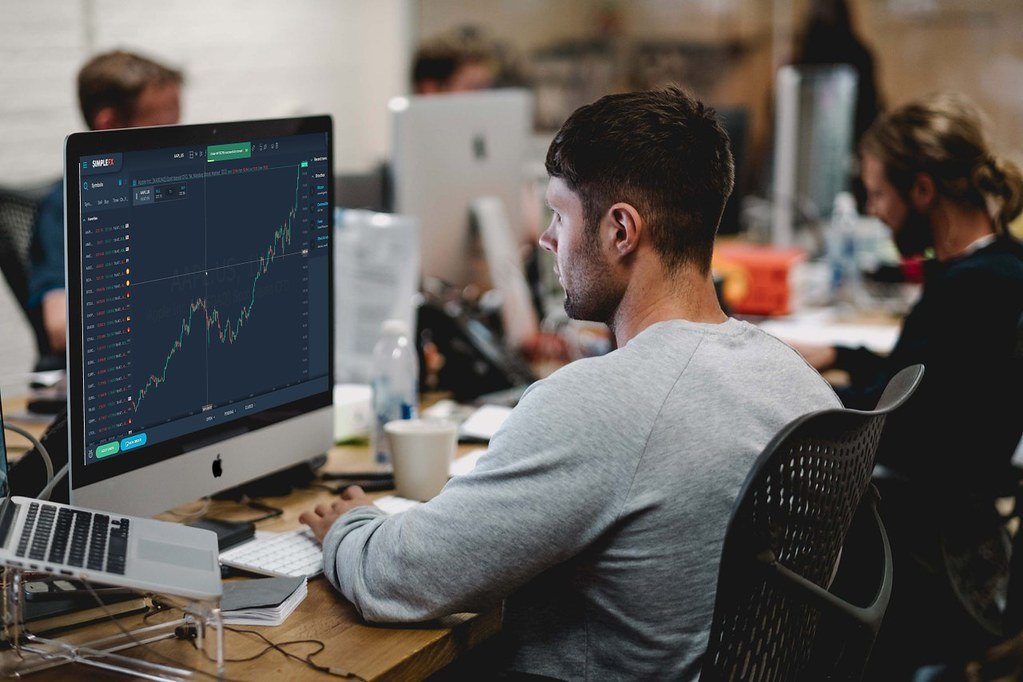 A trader at a desk watching price charts on a desktop computer