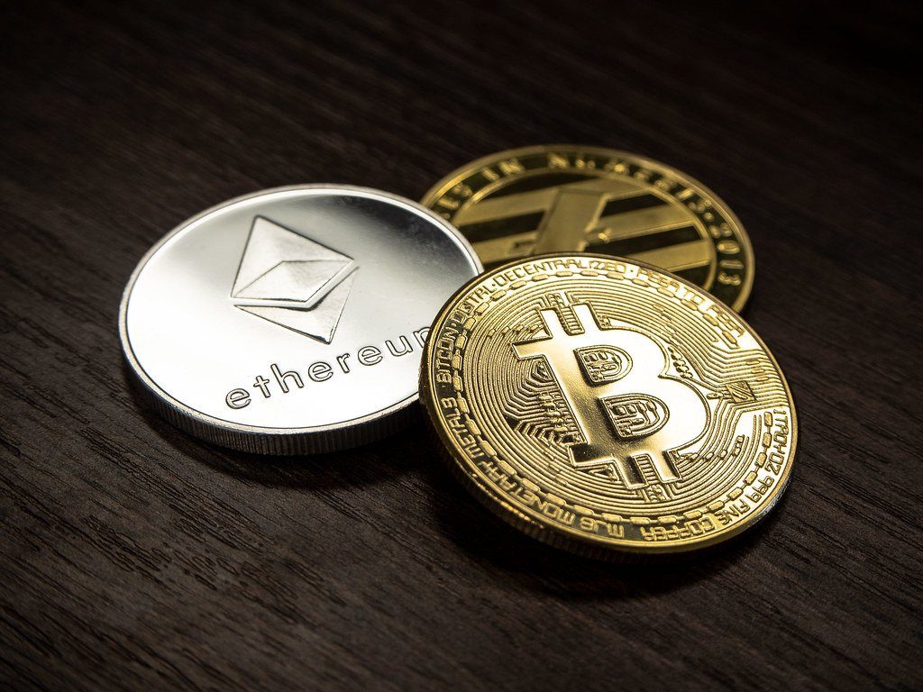 Physical Bitcoin and Ethereum commemorative coins on a dark wooden surface