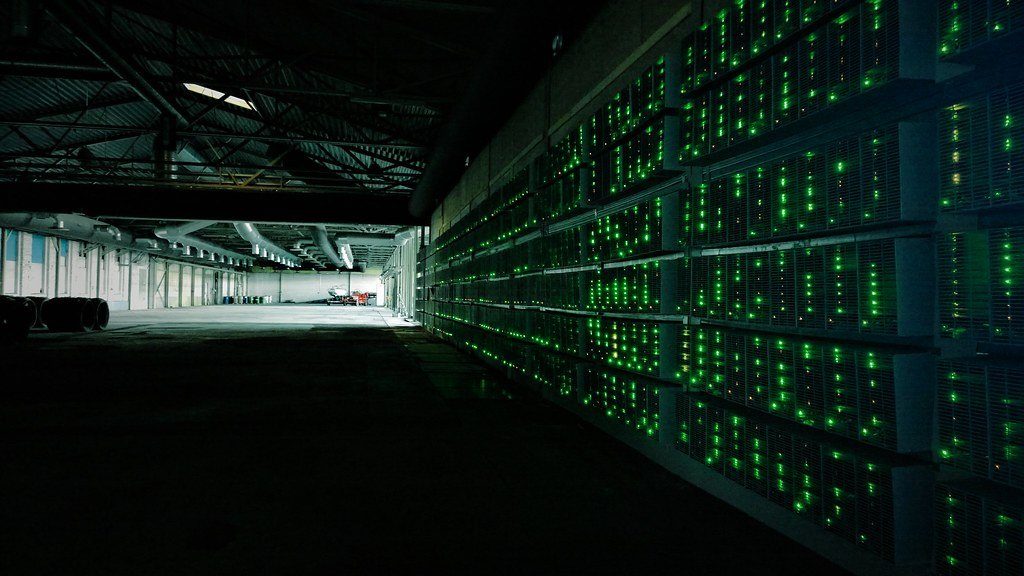 Rows of mining machines with green status lights in a large data hall
