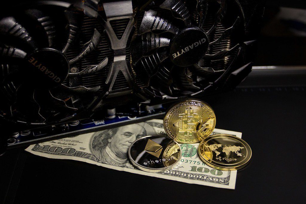Novelty crypto coins resting on dollar bills beside a graphics card